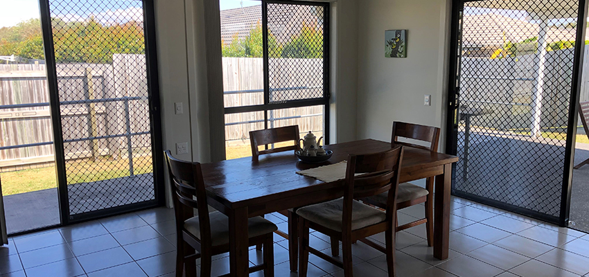Dining room with wooden table and chairs in front of large sliding doors with security screens