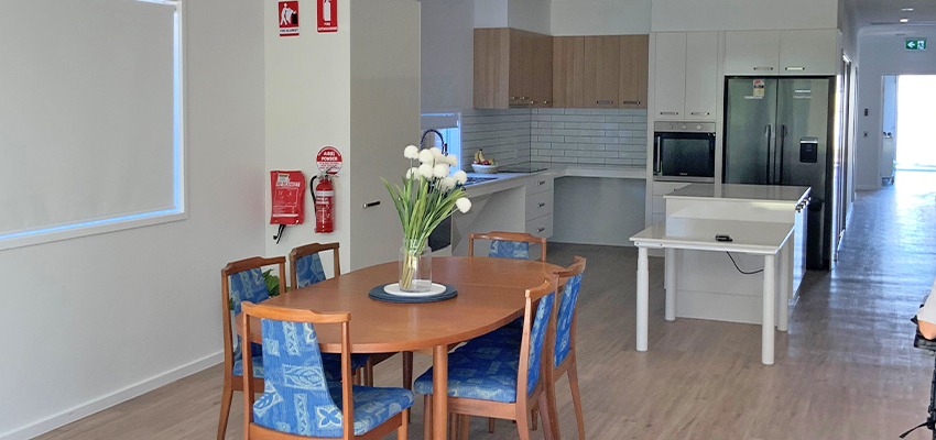 Dining area with table and chairs, kitchen and hallway in the background