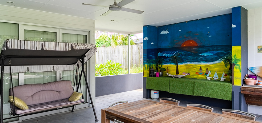 Outdoor patio with a large table and chairs, love seat swing and a mural painted on the wall