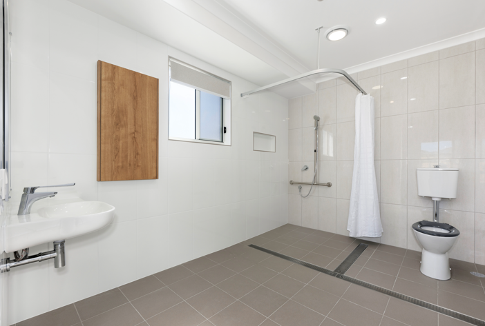 Large accessible bathroom with bright white tiles and grab bar