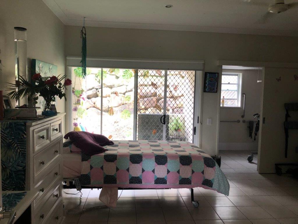 View of bedroom with a large multi-colour blanket over the bed. Behind the bed are sliding glass doors.
