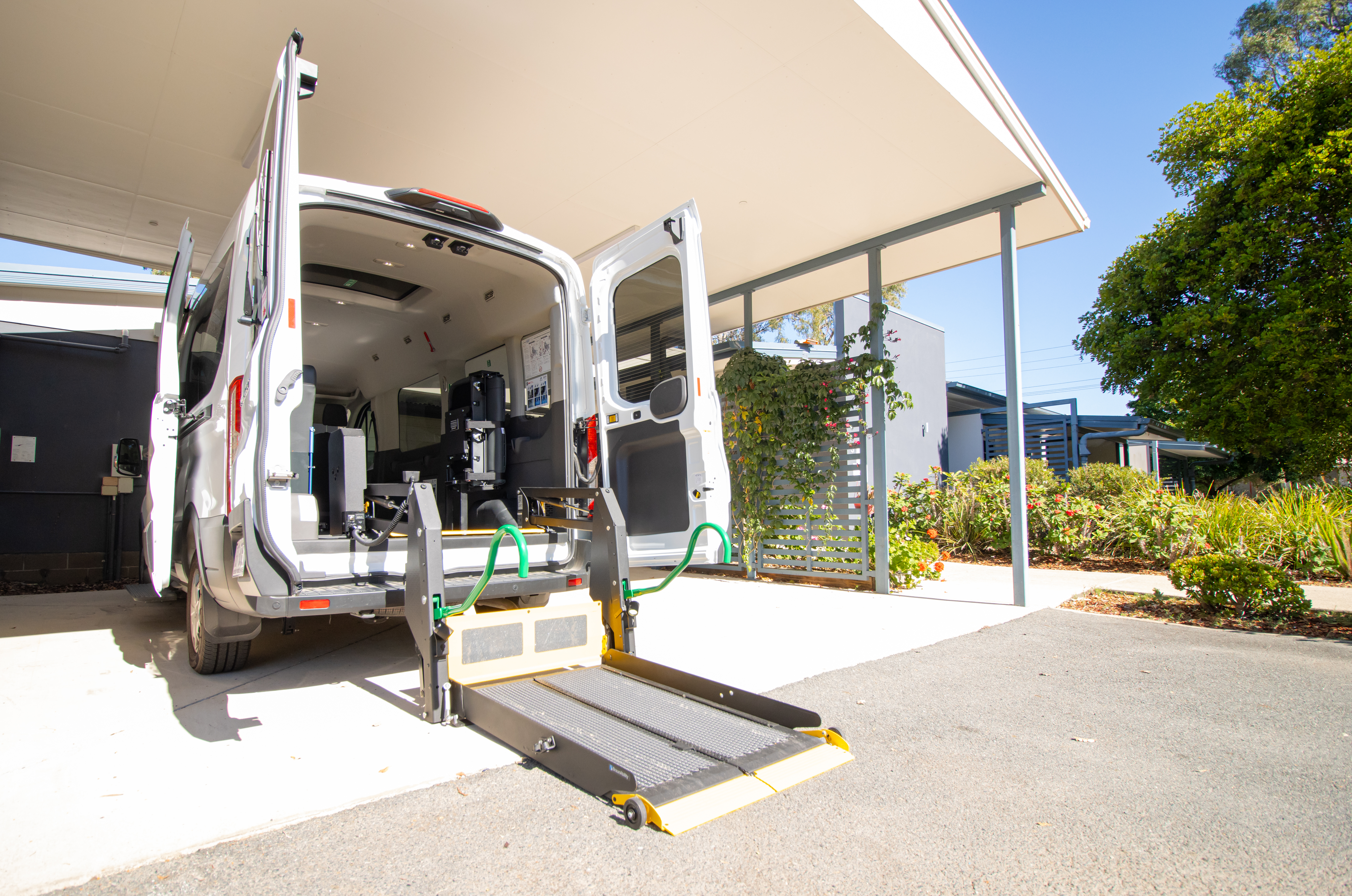 A wheelchair accessible car with its lift down under the carport