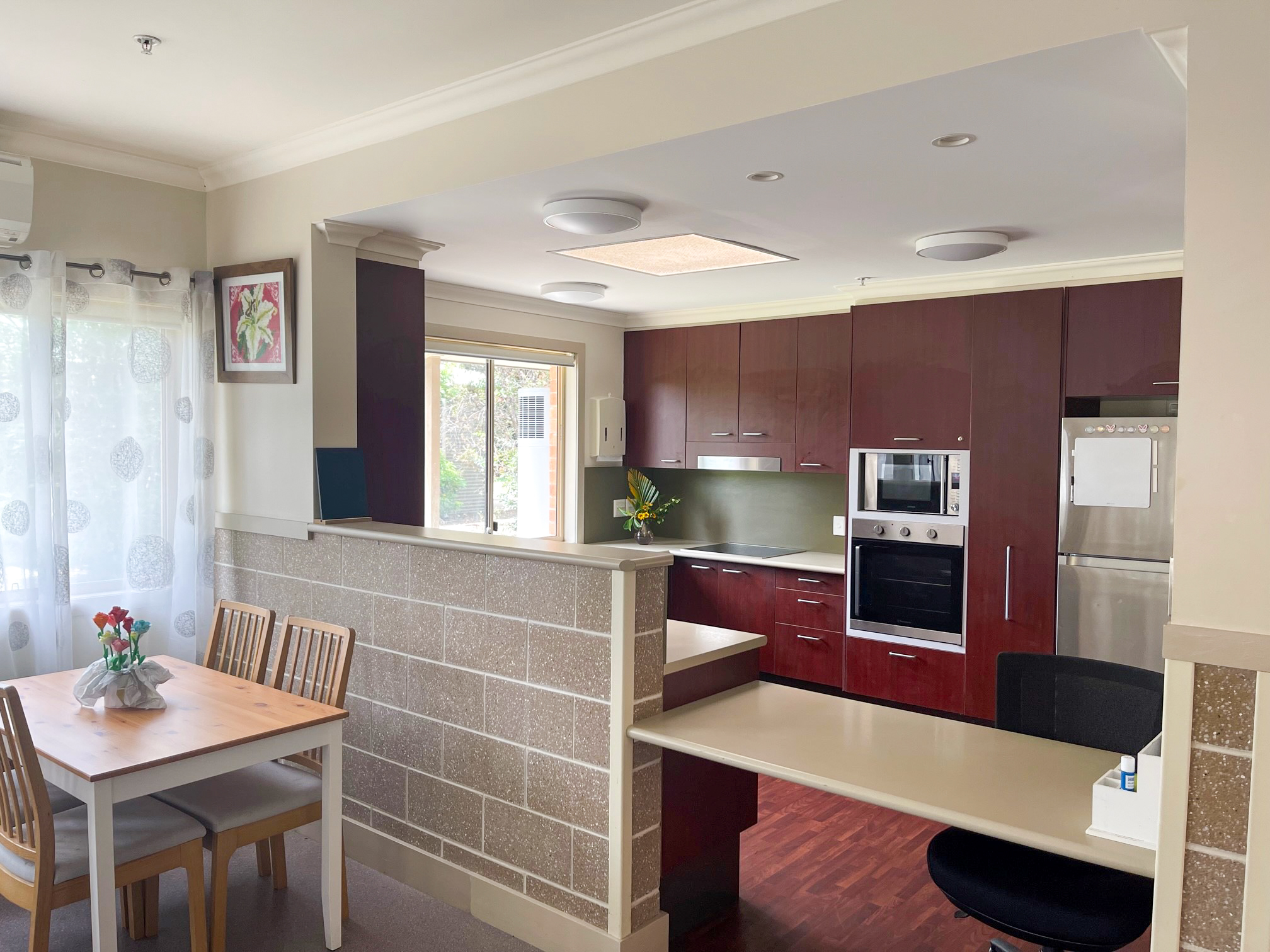 A dining table in front of a nib wall with a kitchen behind