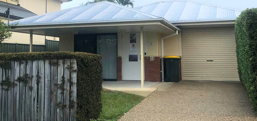 Front entrance of a low set house. Low wooden fence and single garage.