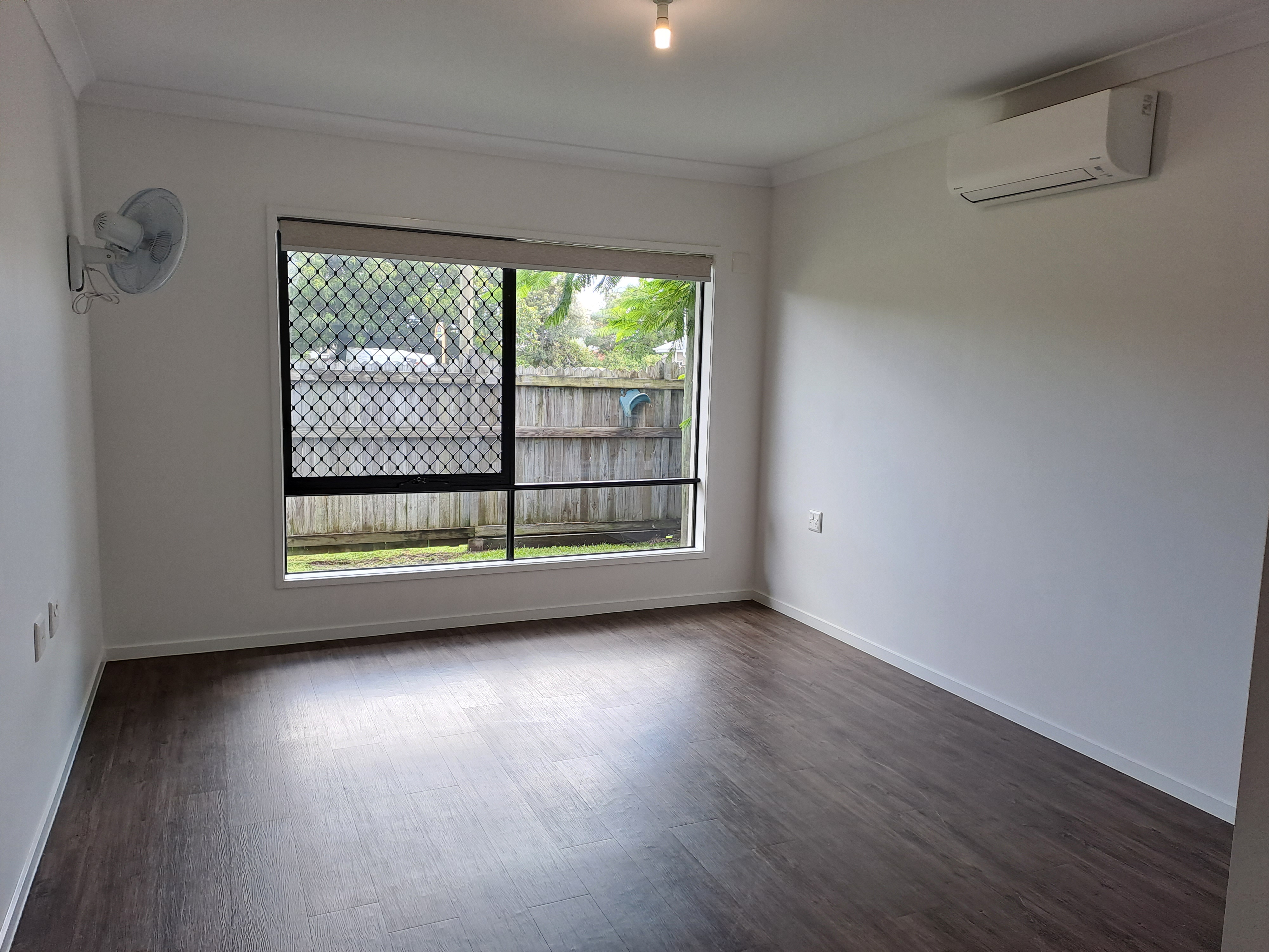 An empty bedroom with light walls and an air con unit