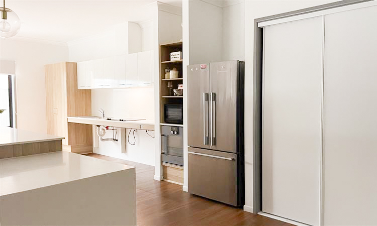 A kitchen with a large fridge and cupboard, and an adjustable benchtop