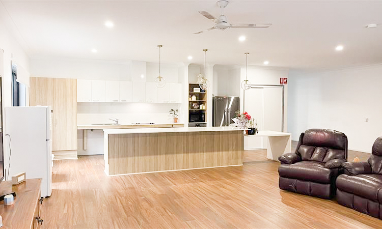A photo of an open plan lounge room with a kitchen behind