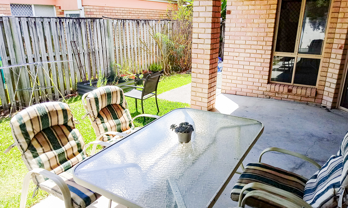 An outdoor patio with a table, chairs and small section of yard