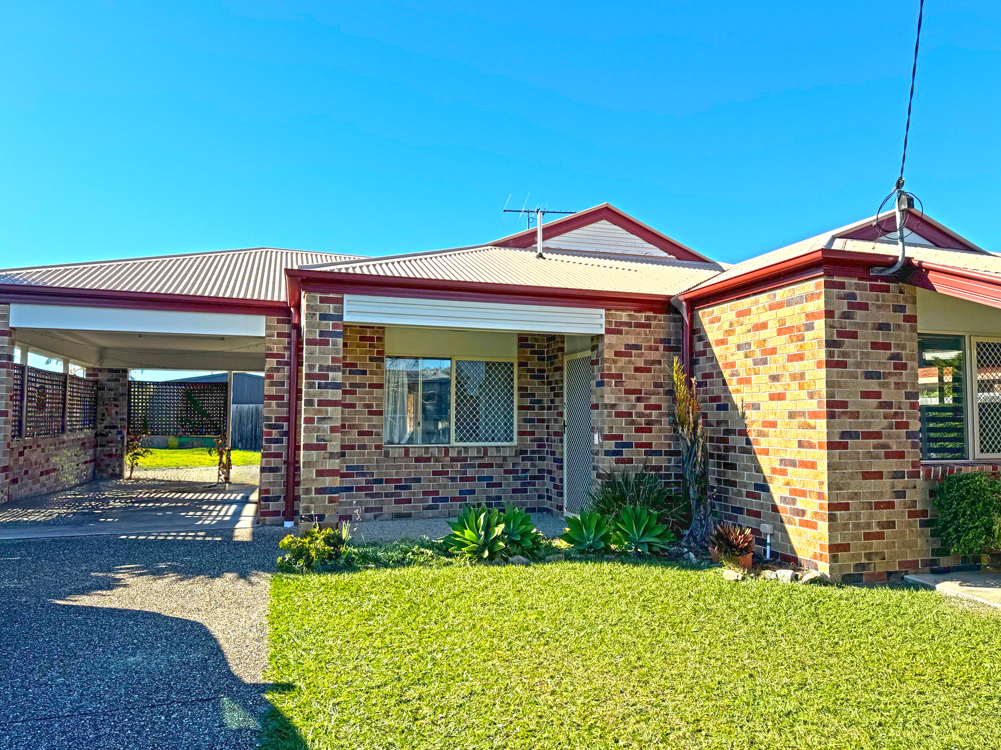 An image of a brick house, with green grass showing in the foreground and a blue sky visible. 