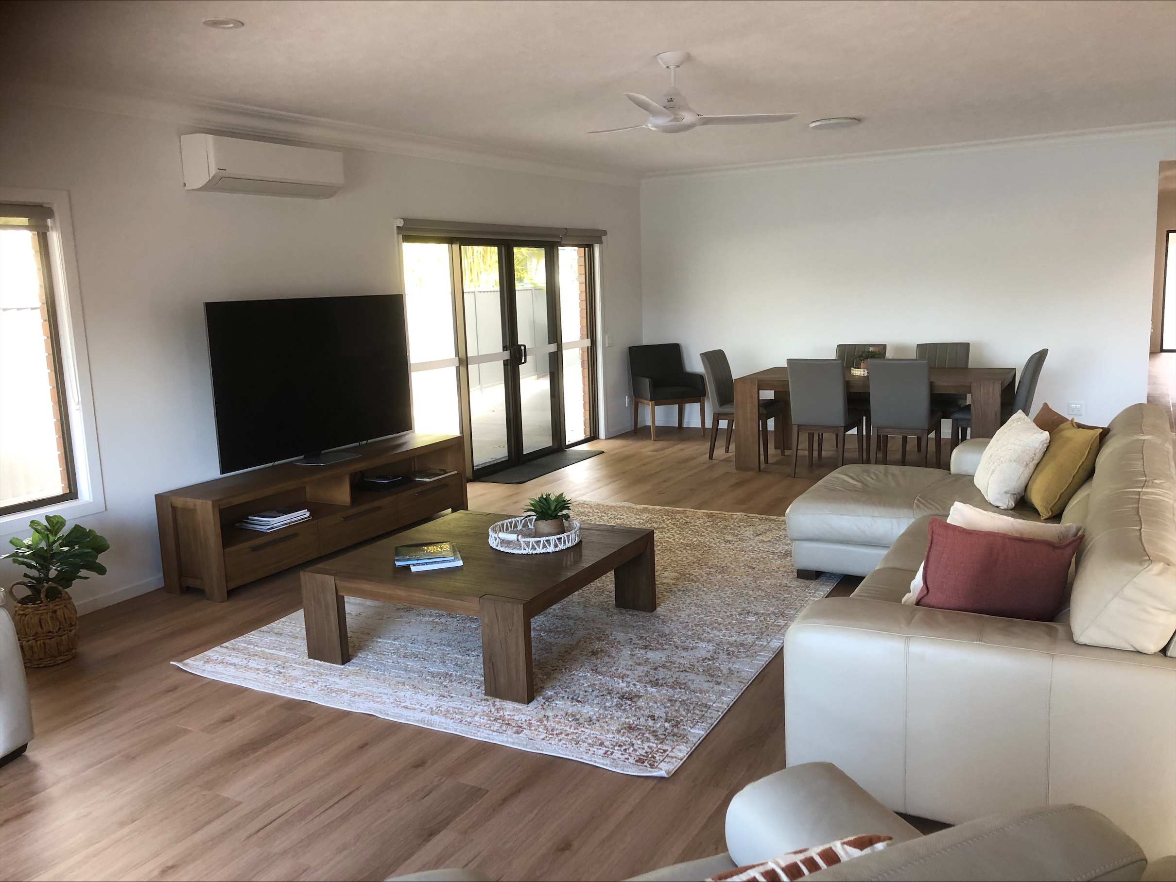 An image showing the lounge room, with large TV, white couch, modern coffee table and wooden flooring