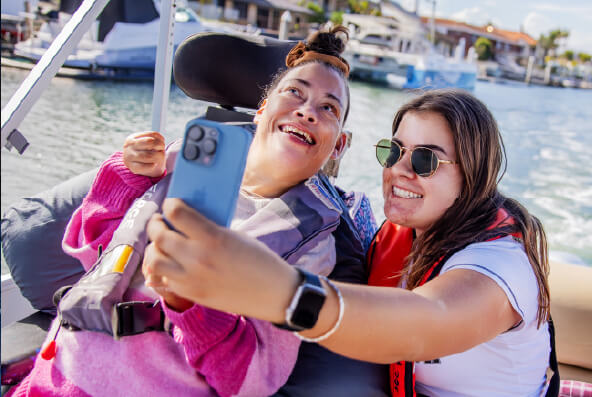 A CPL Client sitting in a wheelchair and a direct support worker pose for a selfie whilst sailing on a boat.  