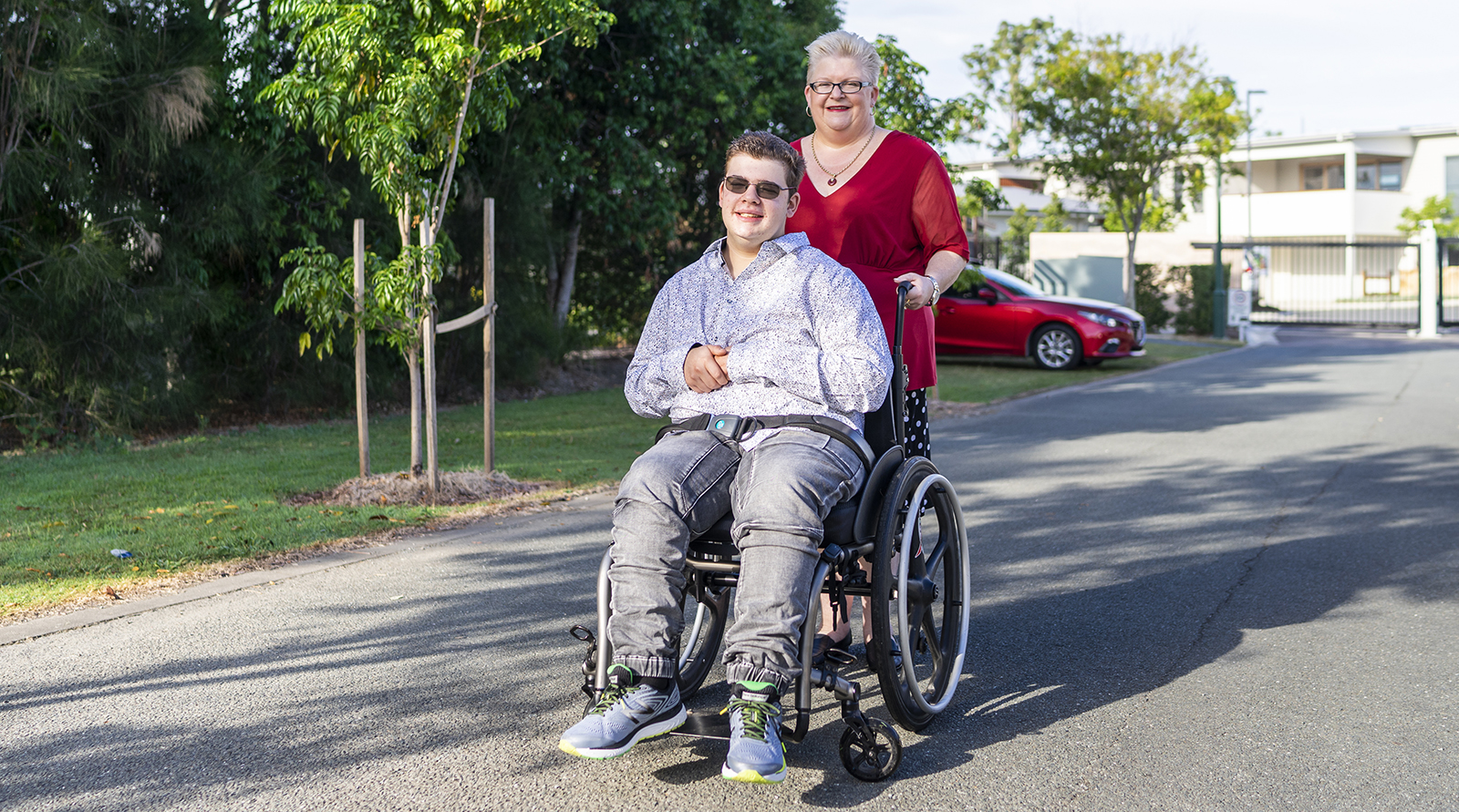Drew seated in a wheelchair, with mum Kelly standing behind him