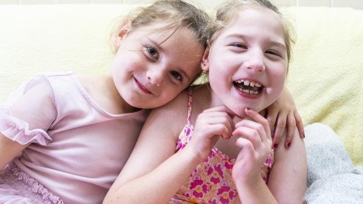 Two young girls sitting together and smiling at the camera