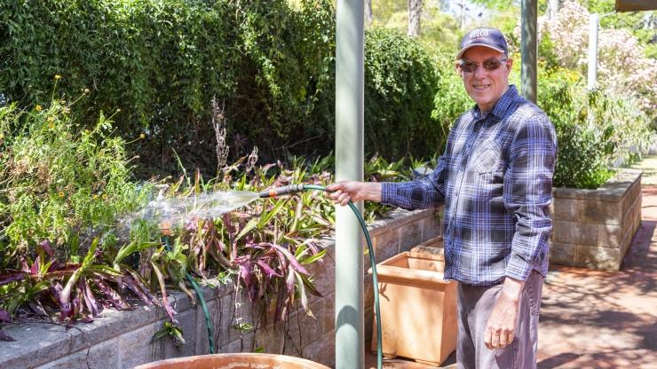 Man standing outside spraying the garden with a hose