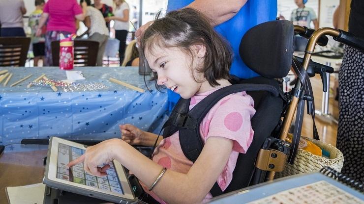 Young girl uses iPad speech device at Camp Have a Chat