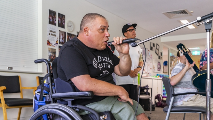 A man in a grey t-shirt singing into a microphone