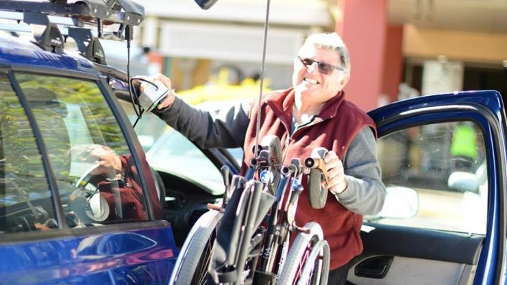 Man standing beside a car, moving a wheelchair into the car