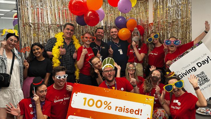 A group of people stood in front of a sparkly gold background. They're all smiling and holding a sign which says "100% raised"