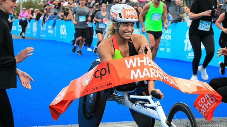 A person in a racing wheelchair crossing the finish line at GCM