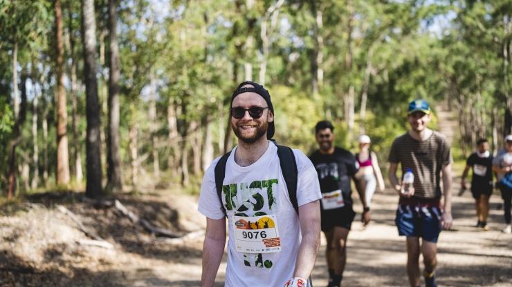 A person in a backwards cap smiling and walking along a bush trail