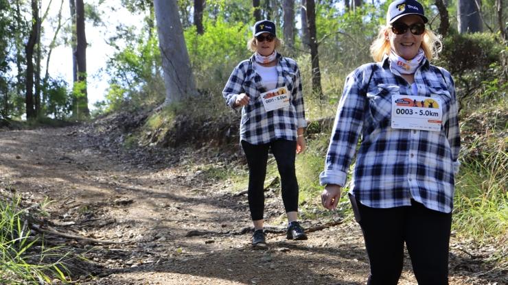 Two people wearing flannel shirts walking through a wood