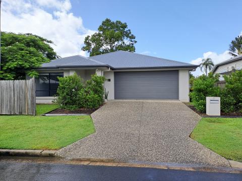 A one-story home with a double car garage with driveway. Green grass and a few bushes at the front, access to the front door is via the driveway.