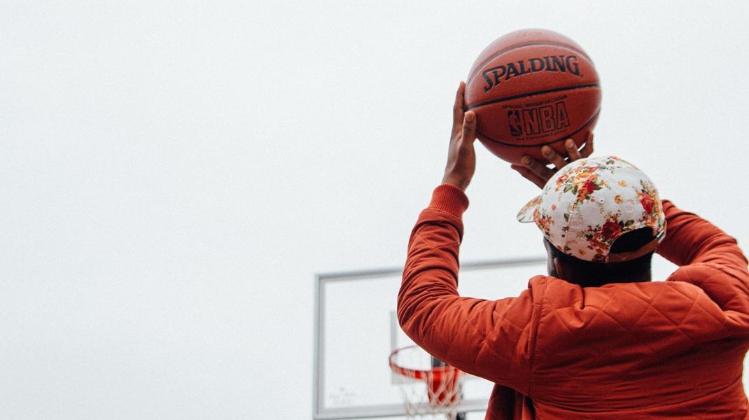 Young boy in an orange jacket holds a basketball above his head