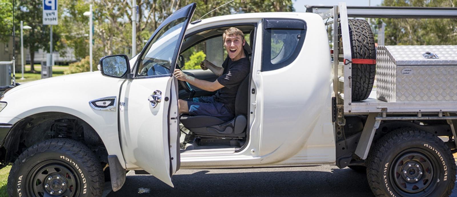 Young man with a disability is driving a ute and smiling