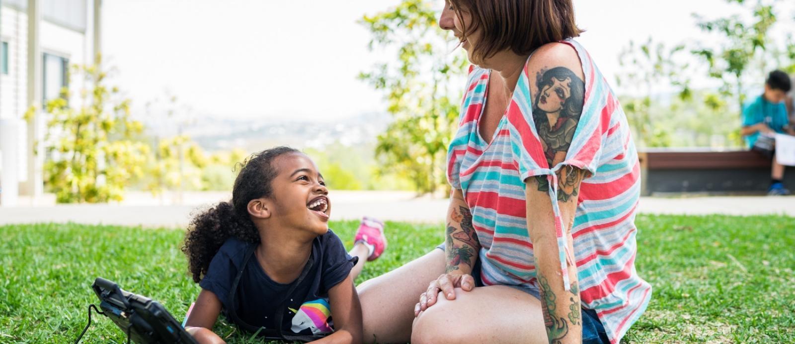 young girl with a disability lies on the grass smiling up at carer
